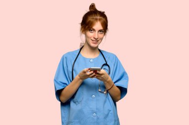 Genç redhead hemşire pembe arka plan üzerinde mobil ileti gönderme