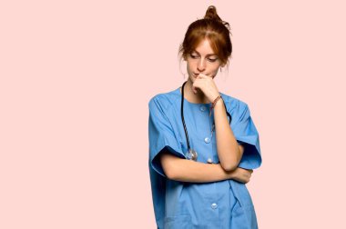 Genç redhead hemşire çene üzerinde el ile pembe arka plan üzerinde aşağı bakıyor