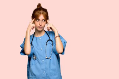 Şüpheleri ve pembe arka plan üzerinde düşünme genç redhead hemşire