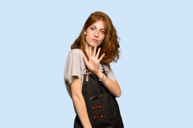 Beş parmak ile mavi arka plan üzerinde sayma önlük ile genç Kızıl saçlı kadın