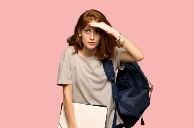 Bir şey üzerinde pembe arka plan bakmak için genç redhead öğrenci uzakta el ile seyir