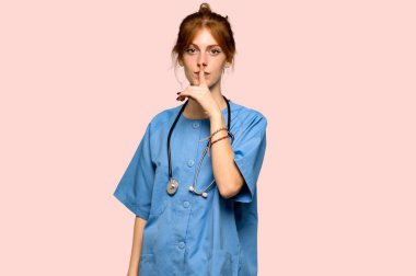 Bir işaret parmağını ağzına pembe arka plan üzerinde koyarak sessizlik jest gösteren genç redhead hemşire