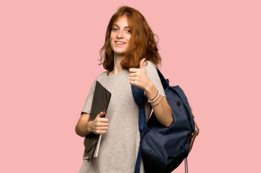 Çünkü iyi bir şey pembe arka plan üzerinde oldu bir başparmak yukarıya hareket veren genç redhead öğrenci