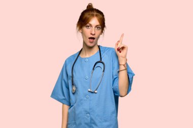 Pembe arka plan üzerinde parmak işaret bir fikir düşünme genç redhead hemşire