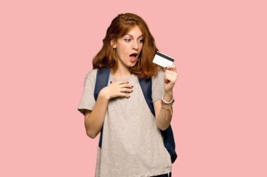 Bir kredi kartı ve sürpriz pembe arka plan üzerinde tutan genç redhead öğrenci