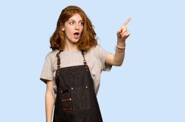 Önlük uzak mavi arka plan üzerinde işaret ile genç Kızıl saçlı kadın