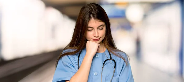 Jovem Enfermeira Olhando Para Baixo Com Mão Queixo Hospital — Fotografia de Stock