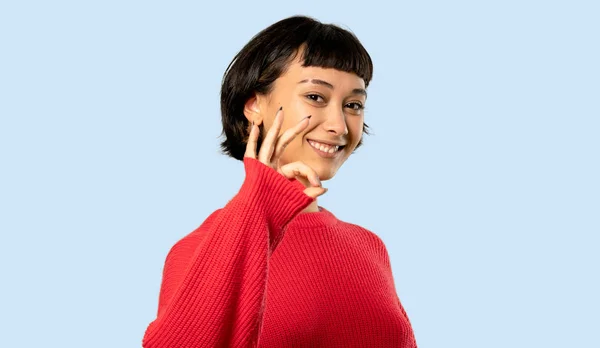 分離の青い背景に指で のサインを示す赤いセーターと短い髪の女の子 — ストック写真