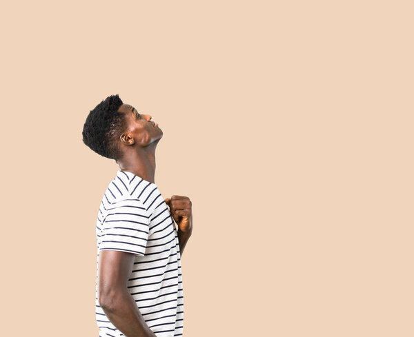 Dark skinned man with striped shirt stand and looking up on isolated ocher background