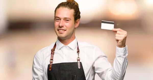 Barber man in an apron holding a credit card in a barber shop