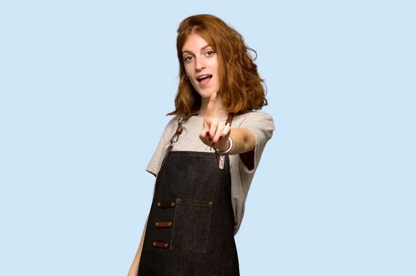 Young Redhead Woman Apron Showing Lifting Finger Blue Background — Stock Photo, Image