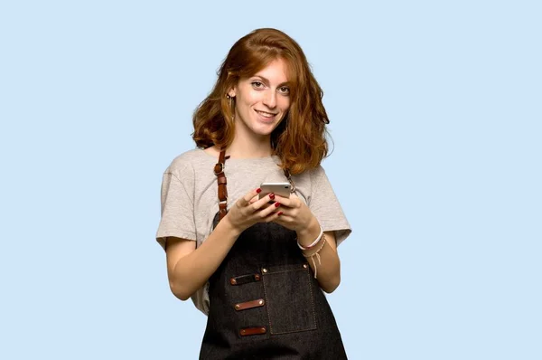 Young Redhead Woman Apron Sending Message Mobile Blue Background — Stock Photo, Image