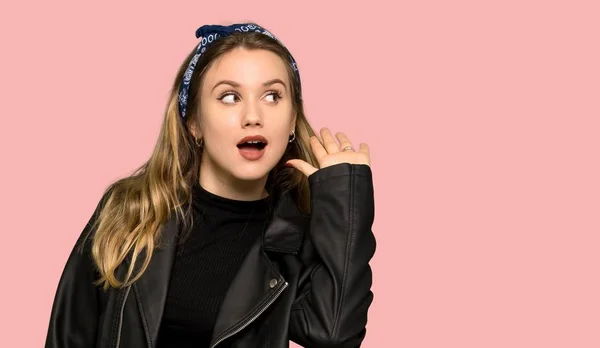 レザー ジャケットの分離 ピンクの背景の耳に手を置くことによって何かを聞くと 代の女の子 — ストック写真