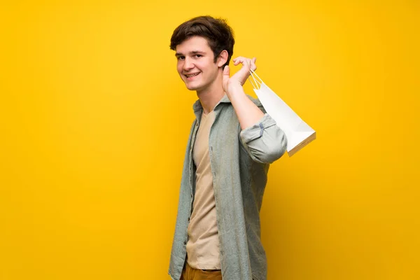 Nastolatek Mężczyzna Nad Żółte Ściany Trzymając Sporo Torby Zakupy — Zdjęcie stockowe