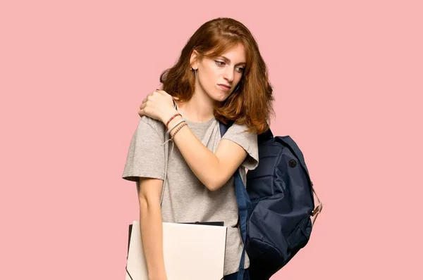Young redhead student suffering from pain in shoulder for having made an effort over pink background