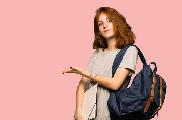 Young redhead student presenting an idea while looking smiling towards over pink background