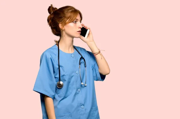 Young Redhead Nurse Keeping Conversation Mobile Phone Pink Background — Stock Photo, Image