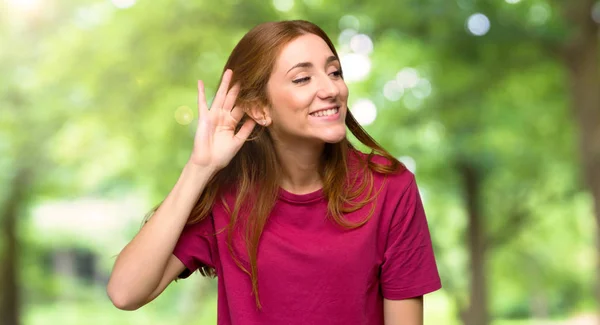 公園で耳に手を置くことによって何かを聞いて若い赤毛の女の子 — ストック写真