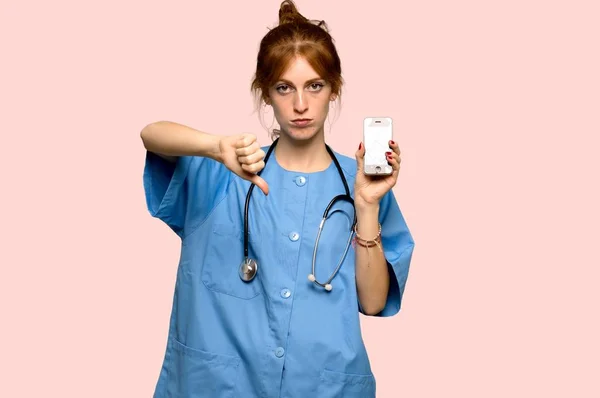 Young redhead nurse with a broken phone over pink background