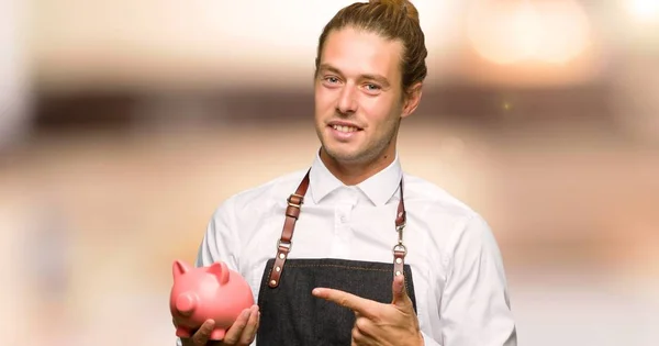 Barber man in an apron holding a piggybank in a barber shop