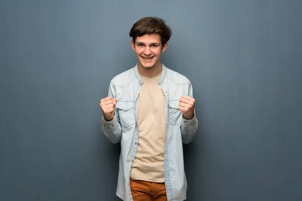 Teenager man with jean jacket over grey wall celebrating a victory in winner position