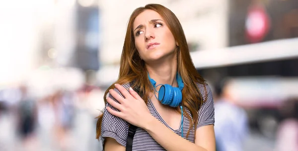 Redhead student woman suffering from pain in shoulder for having made an effort in the city