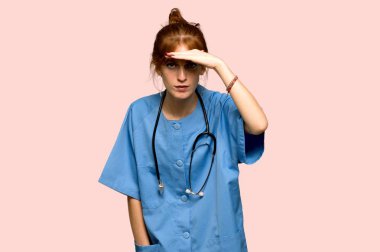 Bir şey üzerinde pembe arka plan bakmak için genç redhead hemşire uzakta yardım arıyorsunuz