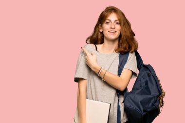 Pembe arka plan üzerinde bir ürün sunmak için genç redhead öğrenci tarafına işaret
