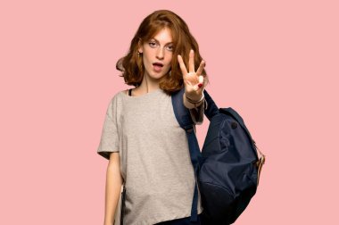 Genç redhead öğrenci mutlu ve sayım üç parmak pembe bir arka plan üzerinde ile