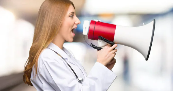 Redhead doctor woman shouting through a megaphone to announce something in lateral position in the hospital