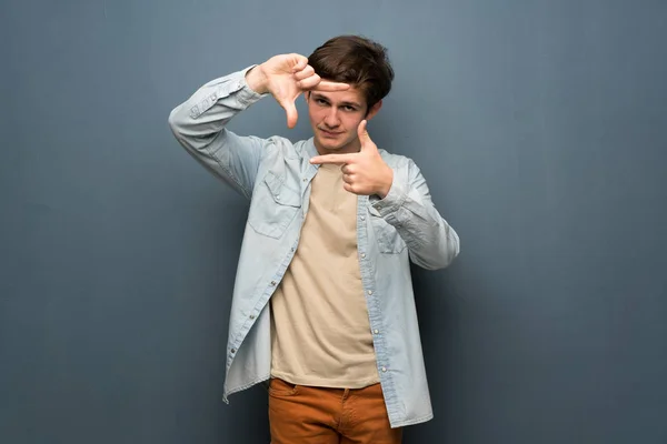 Teenager man with jean jacket over grey wall focusing face. Framing symbol