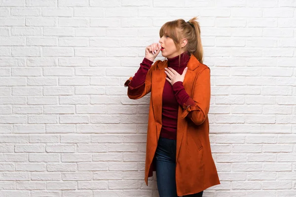 Woman with coat over white brick wall is suffering with cough and feeling bad