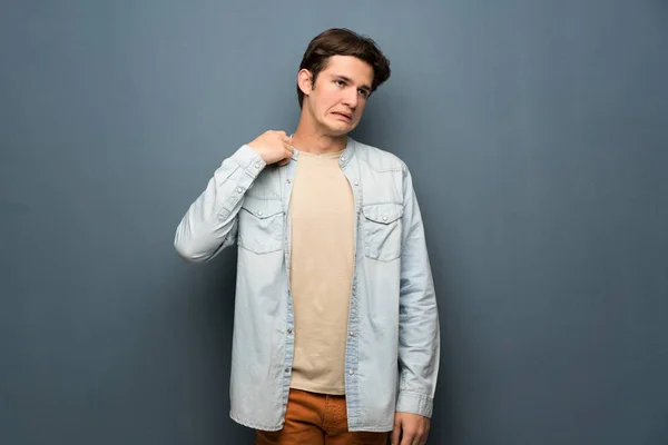 Teenager man with jean jacket over grey wall with tired and sick expression