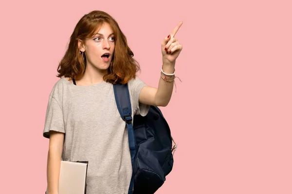 Young redhead student pointing away over pink background