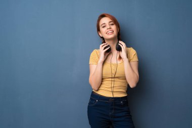 Kulaklıklar ile mavi arka plan genç Kızıl saçlı kadın