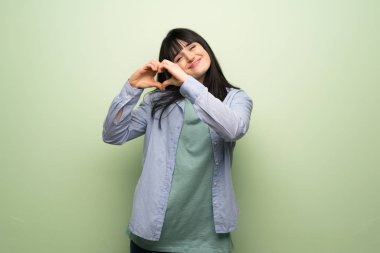 Yeşil duvar eller tarafından kalp sembolü yapma genç kadın