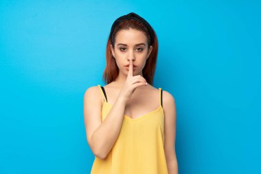 Mavi renkli bir işaret parmağını ağzına koyarak sessizlik jest gösteren genç Kızıl saçlı kadın