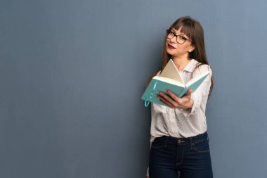 Bir kitap ve birine vererek mavi duvarın üzerinden gözlüklü kadın