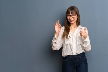 Mavi duvar gösteren ok işareti ile ve jest bir başparmak veren gözlüklü kadın