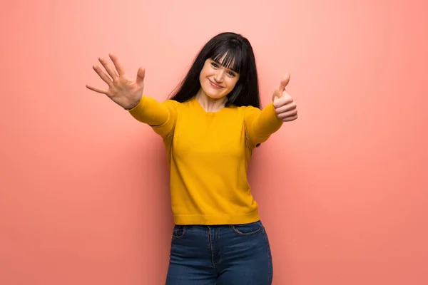 Woman with yellow sweater over pink wall counting six with fingers
