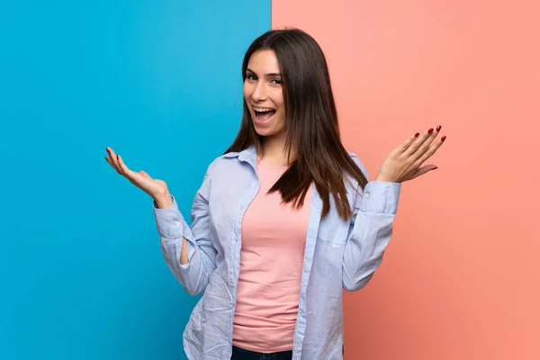 Young woman over pink and blue wall smiling with a sweet expression