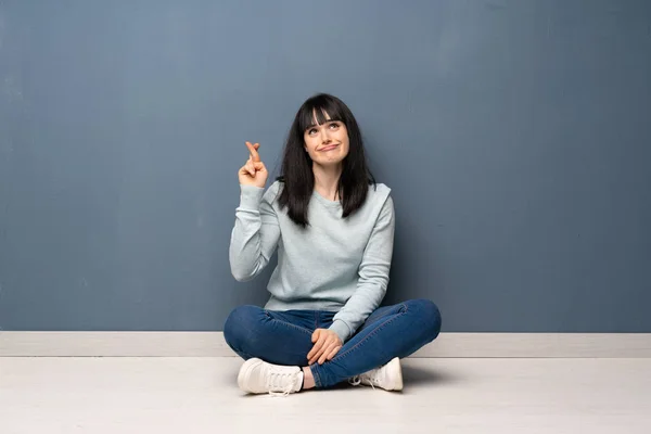 Woman sitting on the floor with fingers crossing and wishing the best