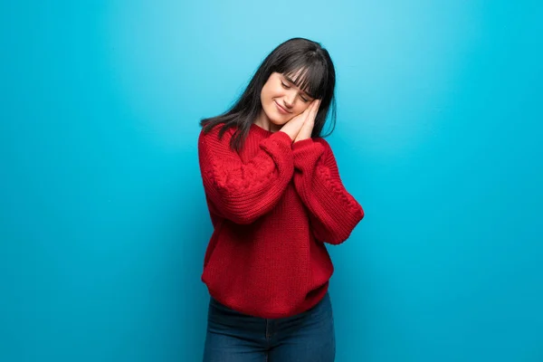 Woman with red sweater over blue wall making sleep gesture in dorable expression