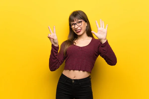 Woman with glasses over yellow wall counting seven with fingers