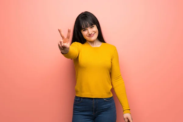 Vrouw Met Gele Trui Roze Muur Glimlachend Overwinning Teken Tonen — Stockfoto