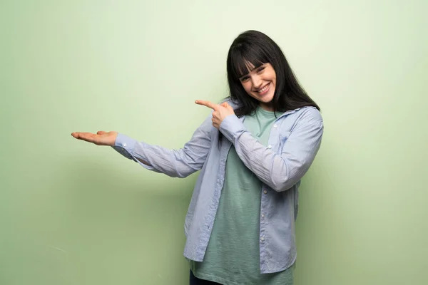 年轻女子在绿色墙上拿着模仿空间想象在手掌插入广告 — 图库照片