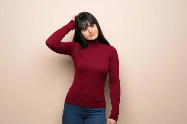 Young woman with red turtleneck having doubts while scratching head