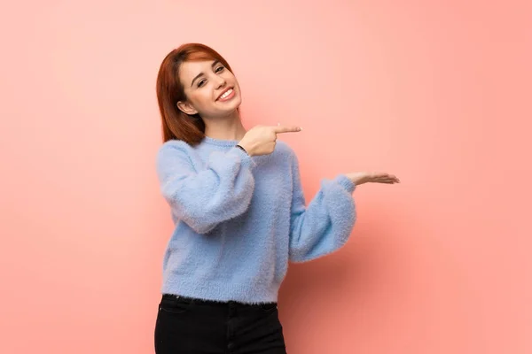 Young redhead woman over pink background holding copyspace imaginary on the palm to insert an ad