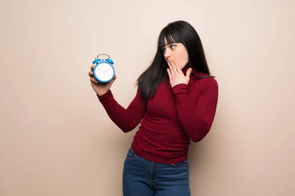 Young woman with red turtleneck holding vintage alarm clock