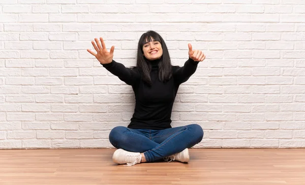 Woman sitting on the floor counting six with fingers